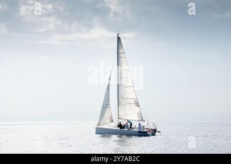 La barca a vela con equipaggio scivola sulle acque calme sotto un cielo limpido Foto Stock