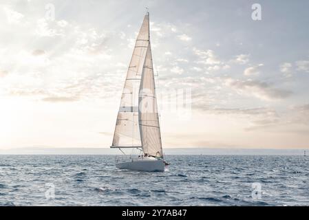 La barca a vela scivola sulle acque calme sotto un cielo pastello al tramonto Foto Stock