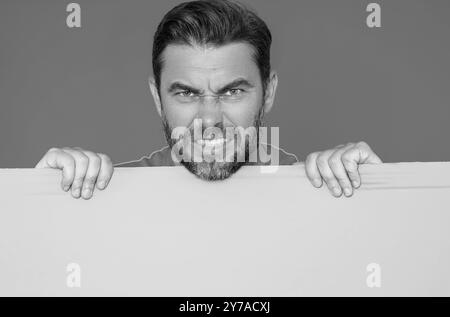 L'uomo arrabbiato ha un cartello bianco. Cartellino pronto per il prodotto. Uomo che mostra un cartello vuoto sullo sfondo isolato dello studio. Lavagna vuota vuota Foto Stock