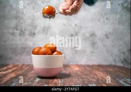 Una ragazza che serve Gulab Jamun in una ciotola con sciroppo dolce. Il Gulab Jamun è un dolce indiano a base di latte, preparato in occasione di feste o feste di nozze. Copia Foto Stock