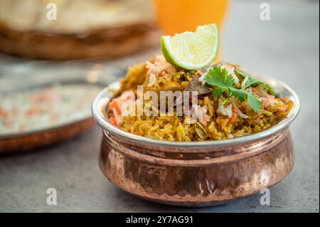 Pulao biryani indiano piccante in ciotola dorata con riso basmati indiano con curry di carne di pollo Ramadan Kareem, Eid. Recipiente da portata in ottone con dorso bianco Foto Stock