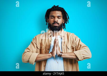 Giovane uomo africano attento in abbigliamento casual che meditava su sfondo blu Foto Stock