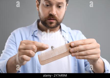 Uomo triste che prende i capelli persi dal pettine su sfondo grigio, primo piano. Problema di alopecia Foto Stock