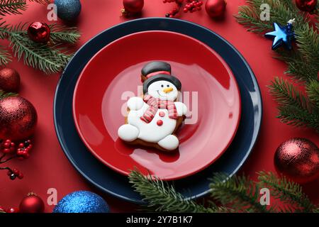 Deliziosi biscotti a forma di pupazzo di neve e decorazioni natalizie sul tavolo rosso Foto Stock