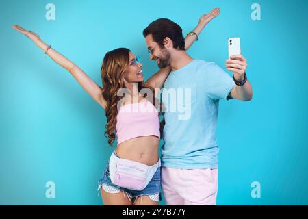 Bella giovane coppia sorridente che fa selfie stando in piedi su sfondo blu Foto Stock