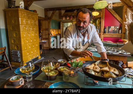 Lo chef René Bobzin prepara il pesce disossato con vari piatti di patate nella cucina del Bauernstube di Bobzin e li presenta personalmente al tavolo della cena. Dewichower Straße, Usedom-Süd, Meclemburgo-Vorpommern, Germania Foto Stock