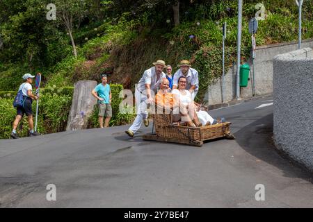 Turisti e turisti che si divertono facendo un giro sulle tradizionali slitte da slittino con cesto di vimini a Monte, Funchal, sull'isola portoghese di Madeira Foto Stock