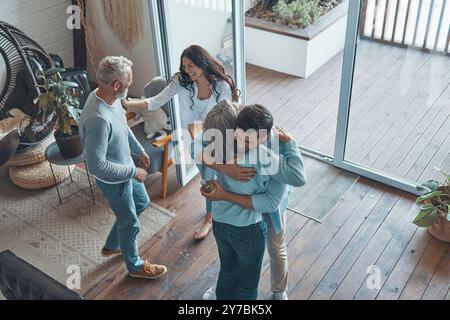 Vista dall'alto dei genitori anziani felici che incontrano giovani coppie all'interno della casa Foto Stock