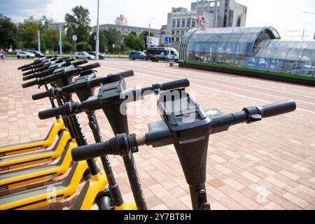 Bielorussia, Minsk - 18 luglio 2024: Una fila di scintillanti scooter gialli ed eleganti neri è ordinatamente parcheggiata in un ampio parcheggio, che mette in mostra la modernità della città Foto Stock