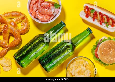 Una foto vivace che mostra bottiglie di birra circondate da vari spuntini e fast food, tra cui un succoso cheeseburger, un classico hot dog croccante Foto Stock