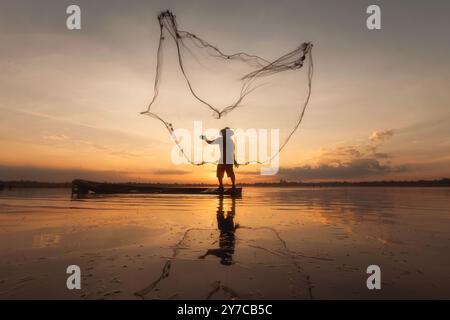 Il pescatore di Laguna con le sue sagome getta la rete al tramonto, mentre il pescatore è in azione al tramonto Foto Stock