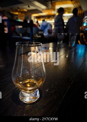 Bicchiere Glencairn di whisky scotch single malt su un tavolo di legno nero in un bar scuro e moderno di una distilleria scozzese Foto Stock