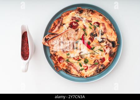 Frittata o frittata italiana con prosciutto, pomodori, formaggio su un piatto blu con fette di pane tostato e salsa rossa. Messa a fuoco selezionata. Copia spazio. Q. Alta Foto Stock