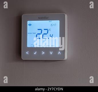 Termostato digitale montato su una parete che mostra una temperatura ambiente di 22,4 °C con pulsanti di controllo sotto il display Foto Stock