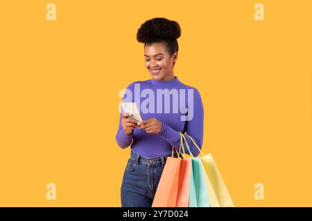 Donna che ama fare shopping e utilizzare lo smartphone su uno sfondo giallo brillante Foto Stock
