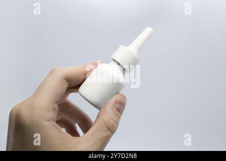 Il giovane è malato usando lo spray nasale per il naso ostruito, spruzzando gocce di naso, tenendo le mani lo spray nasale Foto Stock