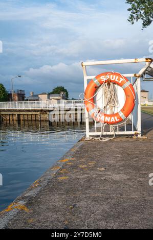 Orange Rescue Life Ring appeso al Waters Edge al canale Sault Ste Marie con una serratura sullo sfondo al tramonto Foto Stock