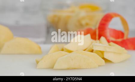Fette di mela e buccia di mela in primo piano su un tagliere bianco sul tavolo da cucina, ricetta per la torta di mele Foto Stock