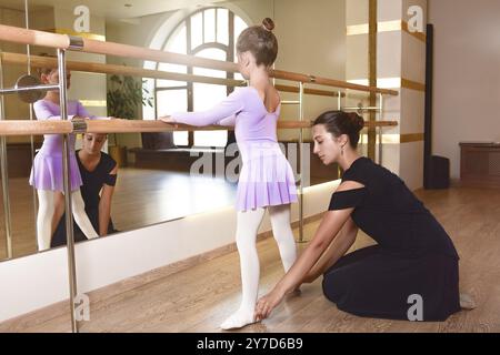 La ballerina studia con l'insegnante di balletto nella scuola di danza classica. L'addestratore femminile di ballo sta insegnando la ragazza del capretto a fare la posizione coreografica wit Foto Stock