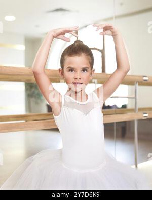 Graziosa piccola ballerina in piedi con le mani in alto in un abito da esibizione. Sta sognando di diventare una ballerina professionista. Scuola di danza, balletto Foto Stock