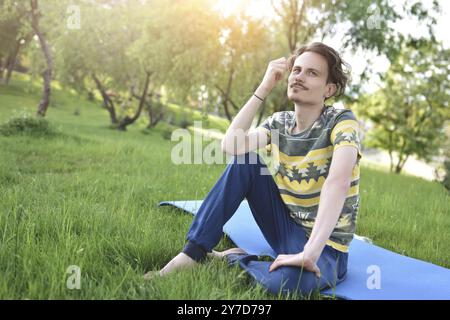 Un bell'elegante ragazzo ama la natura e sogna qualcosa seduto nel parco. vista tranquilla. atmosfera estiva Foto Stock