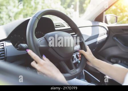 Ravvicinato le mani della donna che tengono il volante mentre si siede nell'abitacolo moderno del veicolo. Ragazza che guida l'auto al concetto di strada Foto Stock