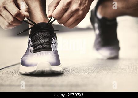 Immagine ritagliata di mani lacci delle scarpe di legatura su sneaker, superficie in esecuzione sullo sfondo. Le mani di uno sportivo con contapassi lacci delle scarpe di legatura su sneaker sportiva. Ru Foto Stock
