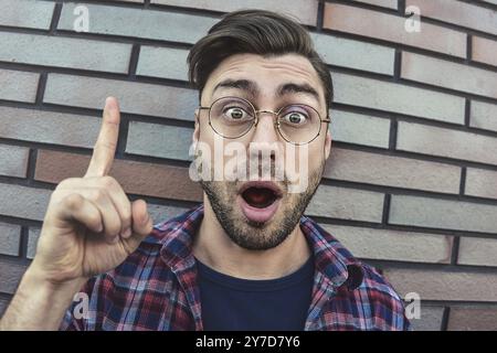Grande idea! Uomo bello mantenendo il dito puntato verso l'alto, mostrando qualcosa sopra la sua testa, rendendo gesto con il dito indice. Eureka, segno della soluzione con Foto Stock