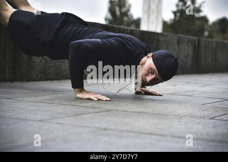 Il giovane sportivo con barba si allena in un parco, facendo una serie di push up all'aperto Foto Stock