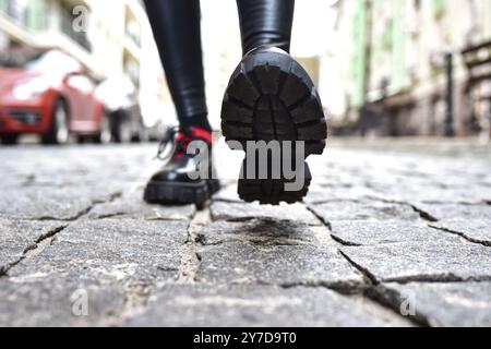 Vista delle gambe femminili con leggings neri e scarpe nere che camminano lungo la strada Foto Stock