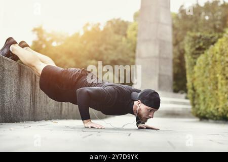 Il giovane sportivo con barba si allena in un parco, facendo una serie di push up all'aperto Foto Stock