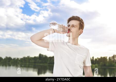 Il giovane beve acqua fresca sul lago e sullo sfondo della foresta. sete estiva. la vista era bellissima Foto Stock