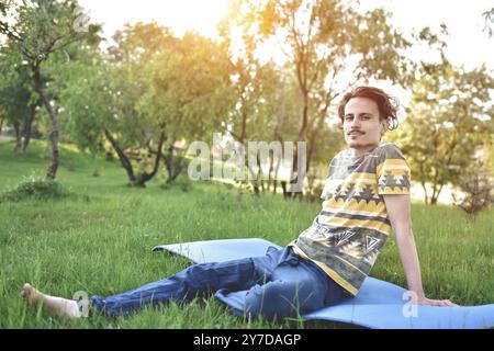 Un bell'elegante ragazzo ama la natura e sogna qualcosa seduto nel parco. vista tranquilla. atmosfera estiva Foto Stock