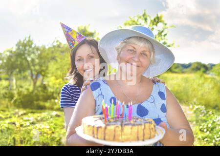 Il compleanno della nonna, che con un sorriso, insieme a sua figlia nel villaggio e tiene una torta di compleanno fatta in casa Foto Stock