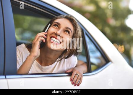 Bella donna con il telefono sorridente mentre si siede sul sedile posteriore in auto Foto Stock