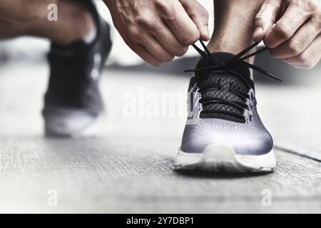 Immagine ritagliata di mani lacci delle scarpe di legatura su sneaker, superficie in esecuzione sullo sfondo. Le mani di uno sportivo con contapassi lacci delle scarpe di legatura su sneaker sportiva. Ru Foto Stock