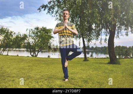 Fitness man che fa esercizio su una gamba isolata nel parco. goditi la natura, lo yoga e la meditazione. pratiche spirituali Foto Stock
