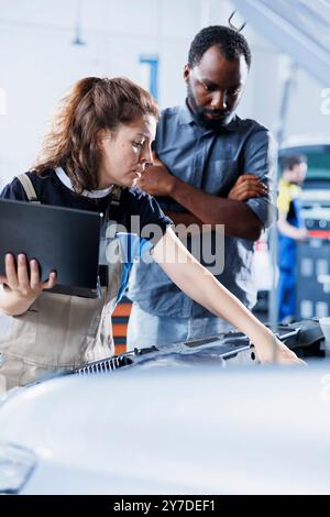 Un cordiale meccanico dell'officina di riparazione conduce annualmente il controllo del veicolo, informando il cliente della necessità di sostituire il motore. Un esperto del settore automobilistico parla con il cliente dopo aver terminato l'ispezione della vettura Foto Stock