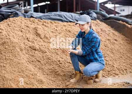 Coltivatore femmina che squatting a mucchio grande di grano esaurito del birwer Foto Stock