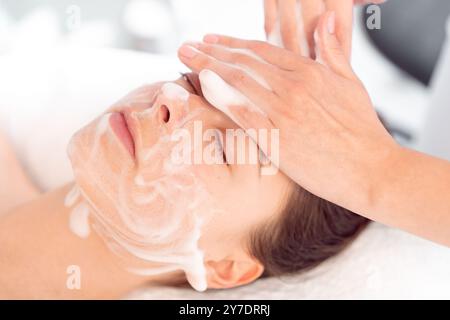 Cosmetologia professionale: Le mani di un terapista che applica crema e massaggia il viso della donna al salone di cosmetologia. La rilassata clientela femminile viene viziata nel centro benessere da professionisti. Foto Stock