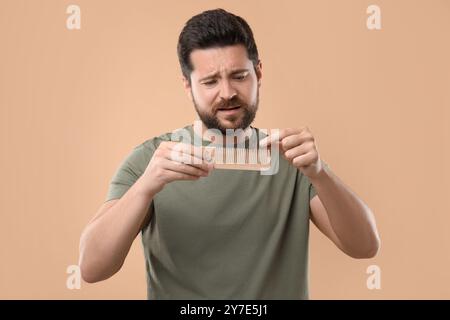 Uomo triste che prende i capelli persi dal pettine su sfondo beige. Problema di alopecia Foto Stock