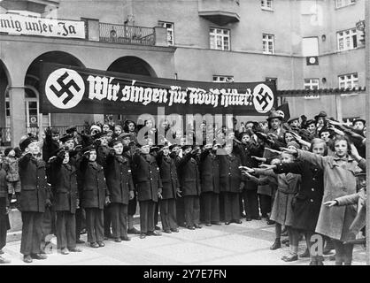 Il coro dei ragazzi di Vienna, riunito sotto uno striscione che recita: "Cantiamo per Adolf Hitler!" Saluti Adolf Hitler e il suo entourage durante la sua prima visita ufficiale a Vienna dopo l'Anschluss. La foto è datata 13 marzo 1938 Foto Stock