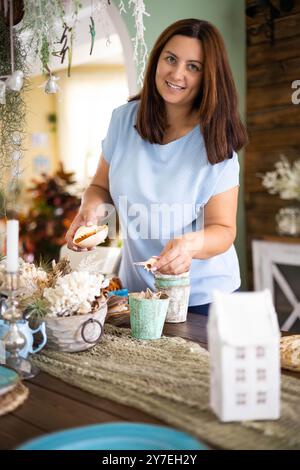 Donna domestica che mette piatti in ceramica blu su supporto wickered che serve la scrivania della cucina a casa Foto Stock