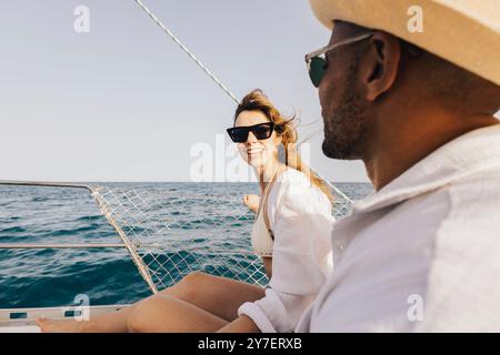 Una coppia allegra si rilassa su una barca a vela sotto il cielo soleggiato, abbracciando la libertà e la gioia del mare aperto. L'atmosfera perfetta per l'avventura estiva. Foto Stock