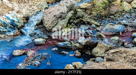 Un flusso d'acqua scorre attraverso un'area rocciosa. L'acqua è blu e le rocce sono piene di colori Foto Stock