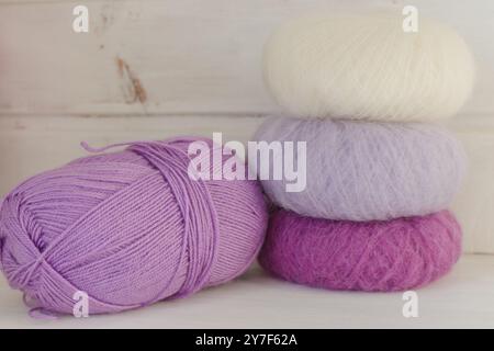 Palline colorate di filato su sfondo bianco. Filato di mohair viola e bianco con spazio di copia. Hobby per lavorare a maglia. Filati multicolori. Negozio di lavoro Foto Stock