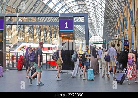 In estate, i viaggiatori in treno con i bagagli delle vacanze camminano sul binario uno della stazione di Kings Cross sotto il tetto storico curvo Camden Londra Inghilterra Regno Unito Foto Stock