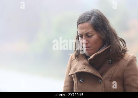 Triste donna di mezza età che guarda giù camminando in inverno in un parco Foto Stock