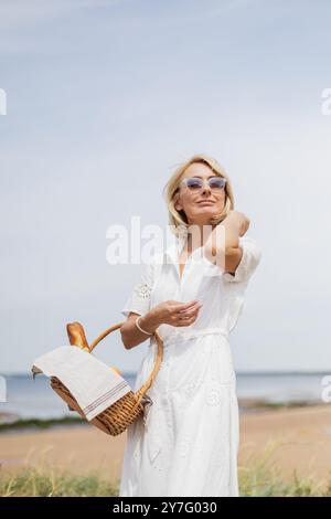 Ritratto di una donna bionda sulla spiaggia di sabbia che tiene in mano un cestino da picnic Foto Stock