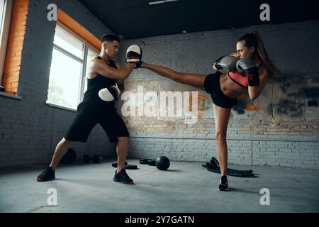 Giovane donna sicura di sé che pratica a calci con il suo allenatore di kickboxing Foto Stock